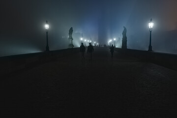 Street lamps and light from them on the old stone Charles Bridge in the night fog and silhouettes of figures