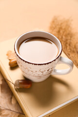 Cup of tasty coffee, book and autumn decor on beige background