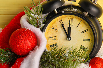 Fototapeta na wymiar Black Christmas alarm clock and fir branches against color wooden background
