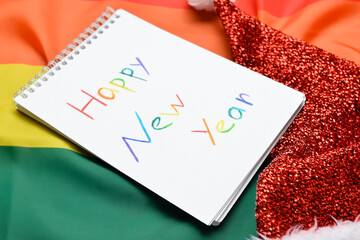 Notebook with text HAPPY NEW YEAR and Santa hat on LGBT flag