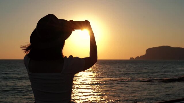 Silhouette of beautiful woman takes picture of sun by smartphone. on beach enjoying sunset sky. happy travel freedom concept . 4k footage