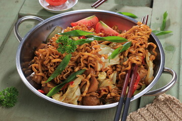Chinese Style Mie Goreng or Stir Fried Egg Noodles is Traditional Indonesian Food with Chicken, Egg, Tomato, Onion, Vegetable and Sweet Soy Sauce in White Plate Served on Wooden White Table.