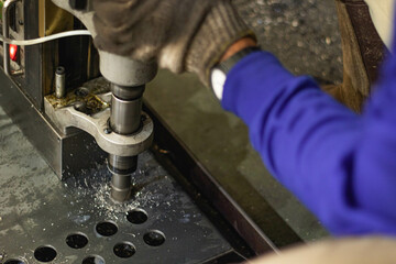 A worker dressed in blue drills holes in the iron.