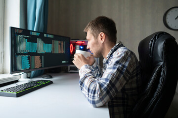 male worker in the office with cup of hot drink sitting in front of computer