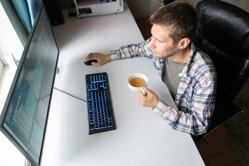 male worker in the office with cup of hot drink sitting in front of computer