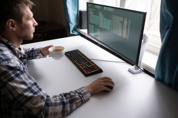 male worker in the office with cup of hot drink sitting in front of computer