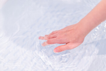 Beautiful woman touching on the surface of water in bathtub to check the water temperature.