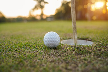 Golf ball on the edge of hole on the green grass with warm tone and sunset.