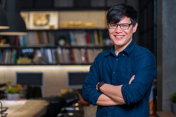 Fototapeta premium Portrait of smiling handsome young Asian business freelance standing in his home office at night with copy space