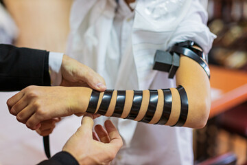 Detail of a moment when a Jewish rabbi puts tefillin on the arm of a thirteen year old boy to say a...
