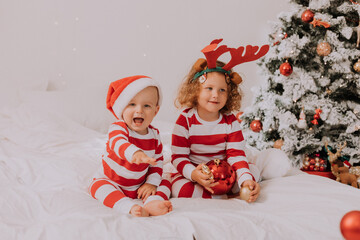 children in red and white pajamas play, have fun, make faces in bed. brother and sister, boy and girl celebrating Christmas. lifestyle. space for text. High quality photo
