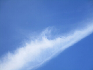 Naklejka na ściany i meble Blue sky with a diagonal white cloud resembling the crest of a sea wave, abstract background