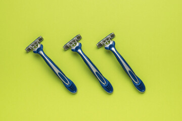 Three blue plastic razors on a green background. Flat lay.