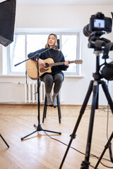 Obraz na płótnie Canvas A young girl plays the guitar, recording video and sound.