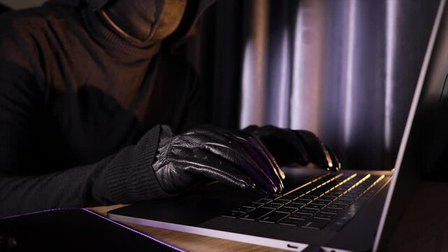Hacker in black, wearing black gloves, writes a virus code on his laptop to social networks.
 Print in a room with lights off late at night.
Steal data from computer systems