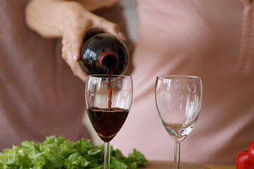 Pair of glasses for red wine woman pouring in kitchen. Romantic dating couple cooking salad for dinner, drinking alcohol, celebrating Valentines day, anniversary. Love, romance concept. Close up