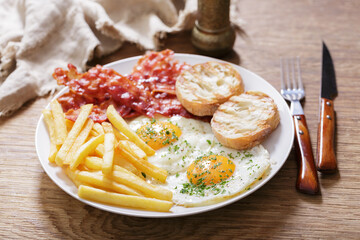 breakfast with plate of fried eggs, bacon, french fries and toast
