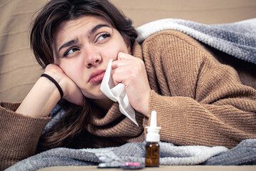 Sick young woman with medicines lies in bed, colds and home treatment.