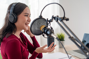 Bright Asian women record a podcast with a microphone and computer camera. A young woman work from...