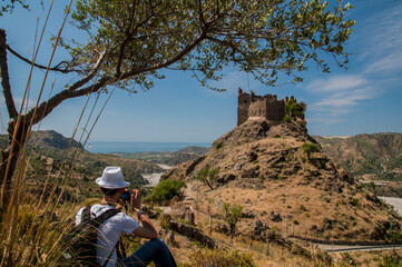 Fotografo seduto sotto un albero con castello Amendolea sullo sfondo