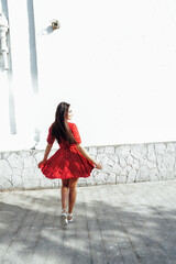 beautiful brunette woman in a red summer dress walks down the street