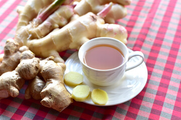 ginger tea in white cup on checkered fabric background Ginger root and sliced fresh ginger plant farm with close-up selected focus.
