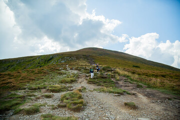 People descend down a large green mountain range. Mountain Hiking