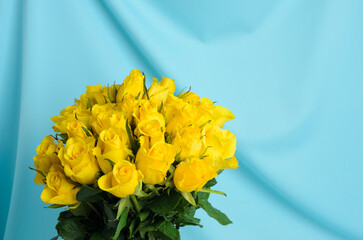 A bouquet of many delicate, yellow roses on a wavy, textured, blue, silk background.