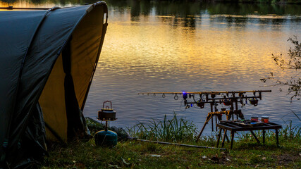Fishing adventures, carp fishing. Angler, at sunset, is fishing with carpfishing technique. Camping on the shore of the lake.Carp Fishing Sunset