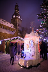 Winter evening on the main square of the city, street by evening lights, before Christmas, New Year. Cat's house on the Christmas Fair. Catholic cathedral, church, tower. Riga, Latvia.