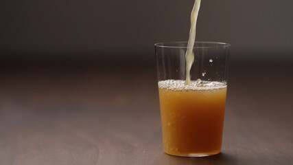 pour orange detox drink into tumbler glass on wood table