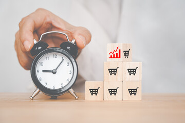 hand holding black analog alarm clock and flips cube with icon red graph and shopping cart symbol for sale volume increase make business growth