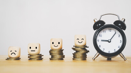 emotion face icon on wooden block on stack of coins and black analog alarm clock