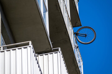 Naklejka premium Bicycle wheel protruding from balcony of multi-storey building, view from below.