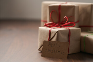 Brown paper gift boxes with red bow and Merry Christmas paper card on walnut table with copy space