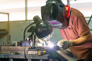 mechanic with welding mask is repairing stamping tool in workshop.
