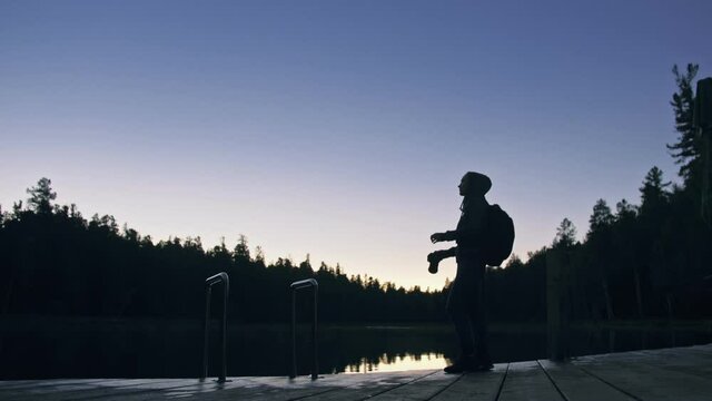 Silhouette traveler photographing scenic view in forest, river. Wood pier. One woman shooting nice dark magic night look. Girl take photo on camera.