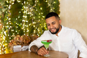Latin American man drinking an exotic alcoholic beverage in an elegant bar. Space for text.