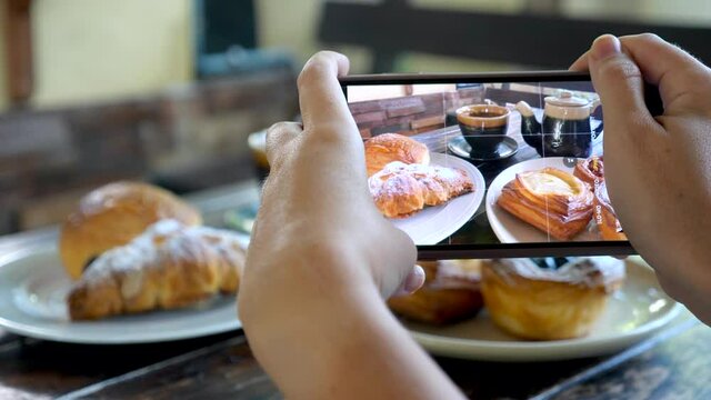 Woman hands taking photos of sweet breakfast with freshly baked danish pastry by smartphone. Food blogger making photoshoot of variety of puff pastries buns in cafe. Delicious snack croissants