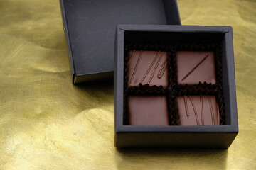 Four pralines in a square black box on a gold metal surface. Small chocolate gift set. 