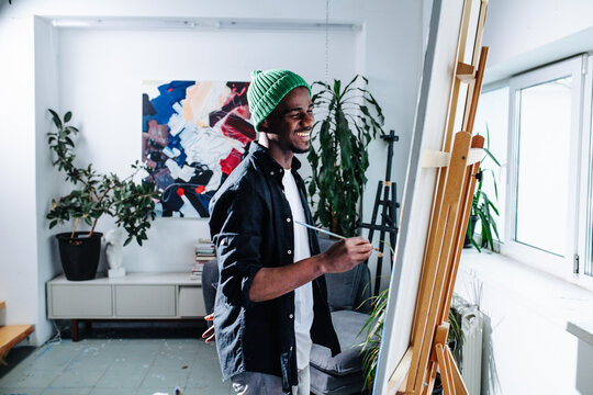 A happy black man painting on an easel inside of his apartment