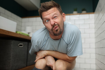 Man with funny facial expression on toilet seat, fulfill natural need