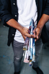 Black artist holding a bundle of brushes, no face.