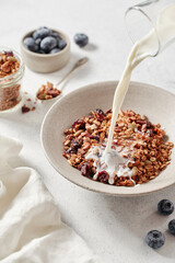 breakfast with granola, milk and berries on a bright table