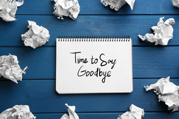 Notebook with phrase Time to say Goodbye and crumpled sheets of paper on blue wooden background,...