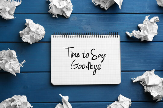 Notebook with phrase Time to say Goodbye and crumpled sheets of paper on blue wooden background, flat lay