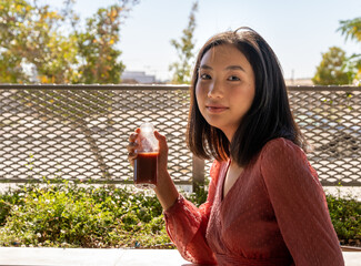 woman posing facing the camera with a glass of healthy drink in her hand on a sunny day