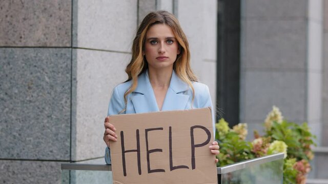 Portrait sad fired poor caucasian millennial business woman standing in city looking at camera holding cardboard sign banner text help asks for work rescue worries about unemployment problem crisis