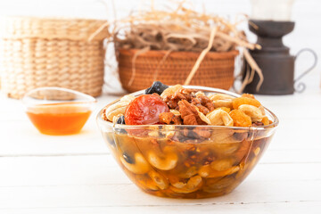 Mixture of walnuts, cashews, raisins, dried apricots and prunes with honey in a glass cup on a white wooden table