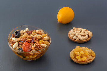 Mixture of walnuts, cashews, raisins, dried apricots and prunes with honey in a glass jar with ingredients and lemon on a gray table